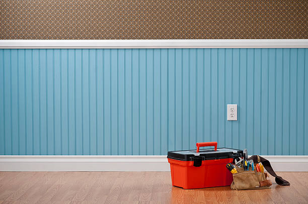 Красный ящик для инструментов и сумка для инструментов стоят на деревянном полу у стены, обшитой синими панелями.